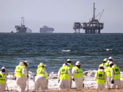 Cleanup workers search for contaminated sand and seaweed in front of drilling platforms and container ships about one week after an oil spill from an offshore oil platform on October 9, 2021, in Huntington Beach, California.