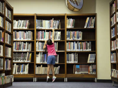 Girl reaching for book on library shelf