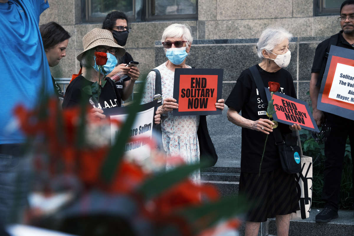 People march with roses and signs reading "END SOLITARY NOW" during a vigil