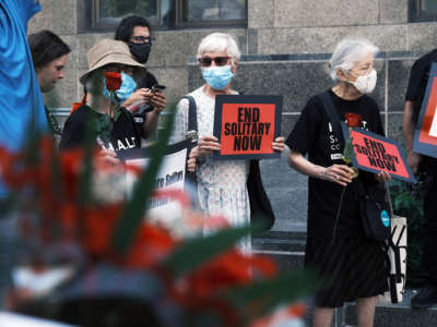 People march with roses and signs reading "END SOLITARY NOW" during a vigil