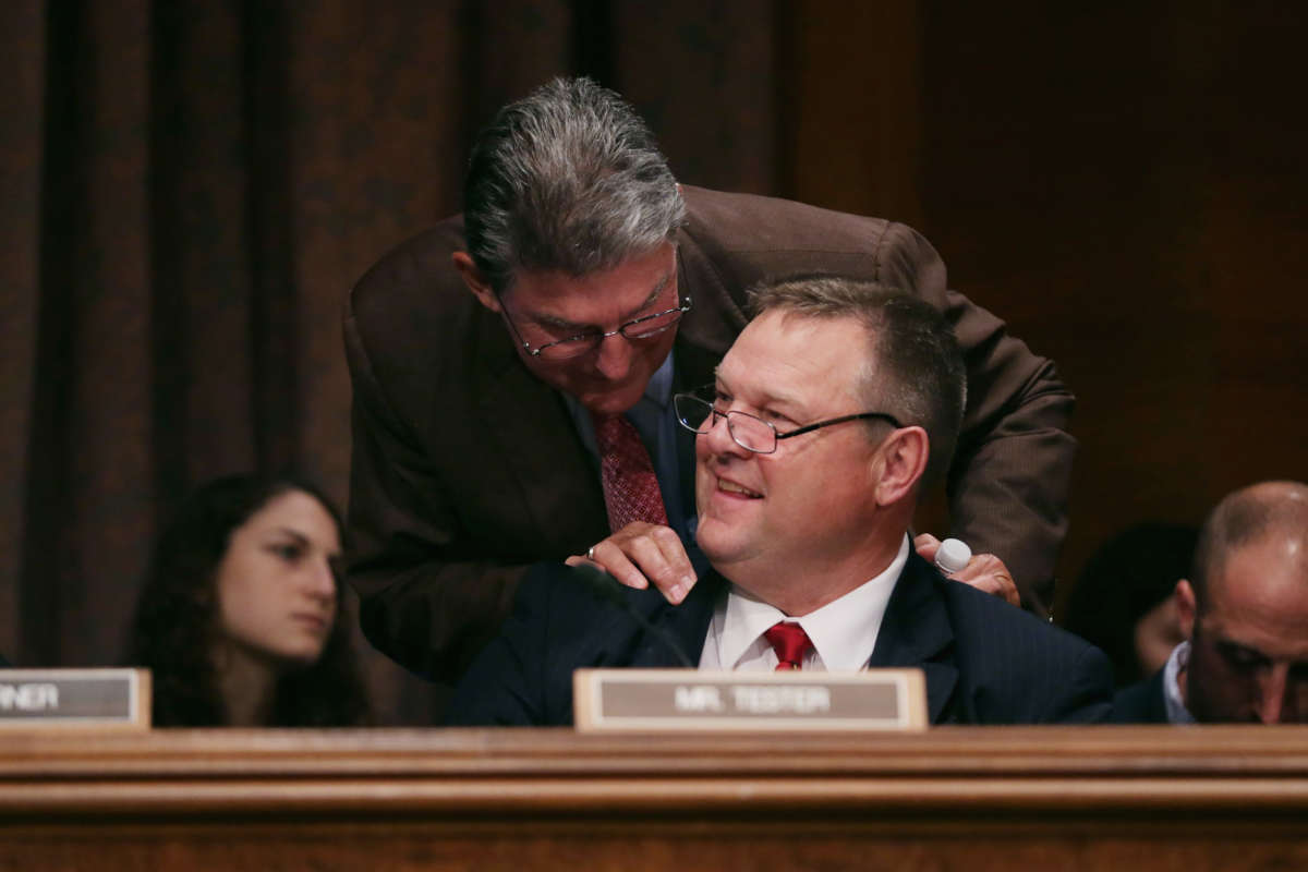 Senators Joe Manchin, left, and Jon Tester visit during a confirmation hearing in the Dirksen Senate Office Building on Capitol Hill on June 17, 2014, in Washington, D.C.