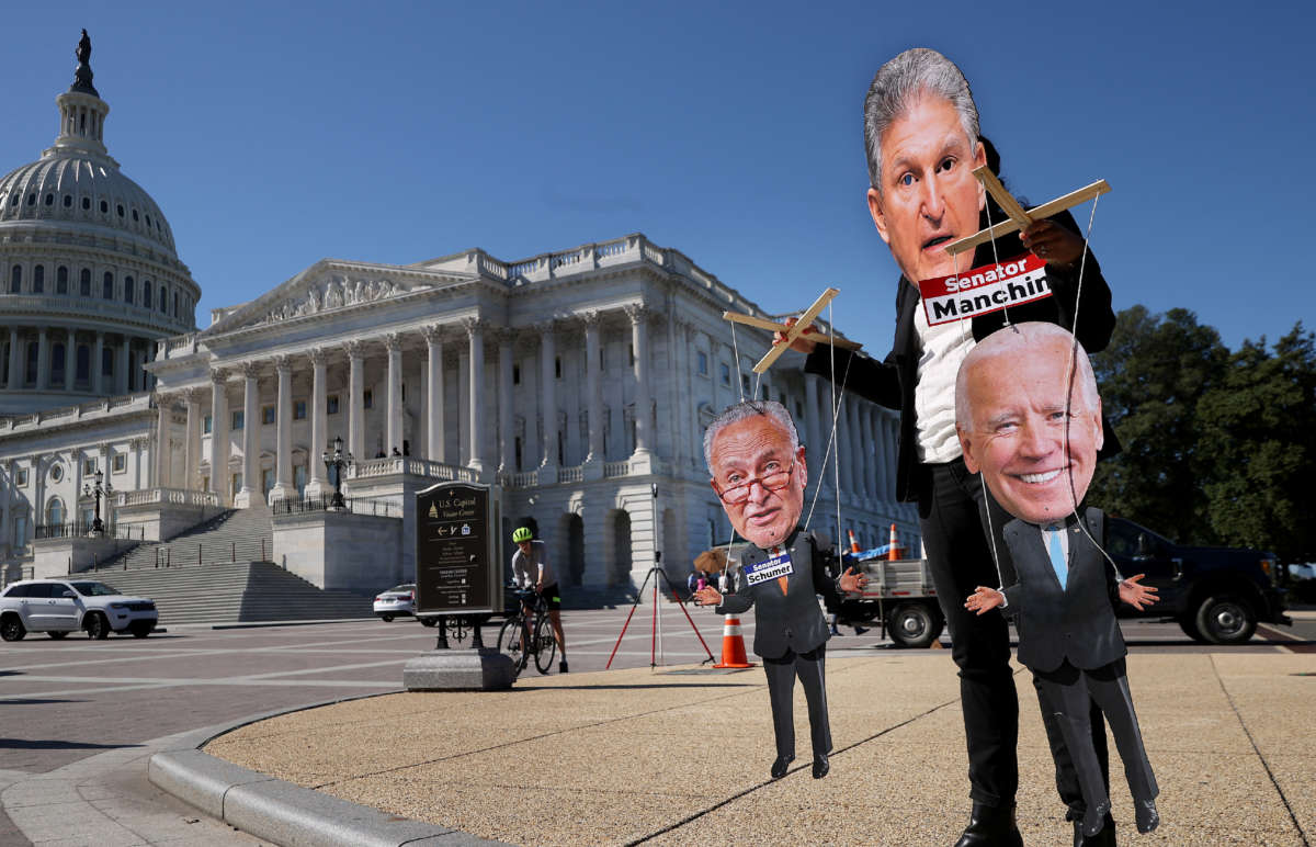 A demonstrator wearing a Joe Manchin mask plays puppet-master to Chuck Schumer and Joe Biden puppets outside the U.S. Capitol