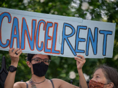 A person holds a sign reading "CANCEL RENT" during an outdoor demonstration