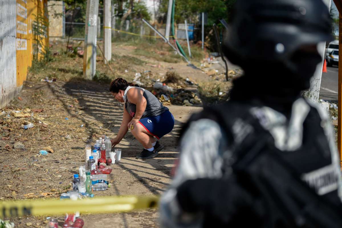 A woman lights candles beside a wall as a police officer stands in the foreground