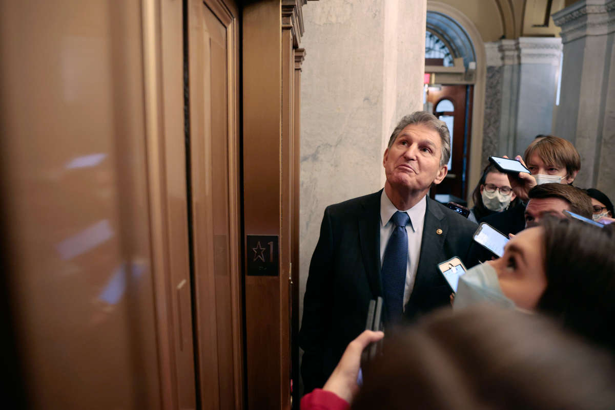Joe manchin looks up at an elevator while surrounded by reporters