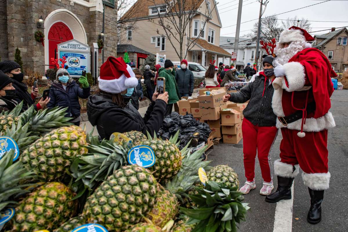 People in Santa hats distribute food as a man dressed as Santa poses for a photo in the foreground