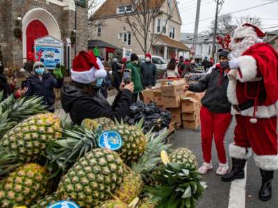People in Santa hats distribute food as a man dressed as Santa poses for a photo in the foreground