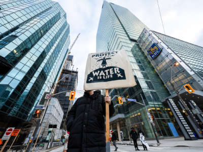 An activist holds up a placard saying, "We Are Here to Protect, Water is Life" during the demonstration. Protesters gather in solidarity with Wetísuwetíen Land Defenders in Toronto, Canada, on December 21, 2021.