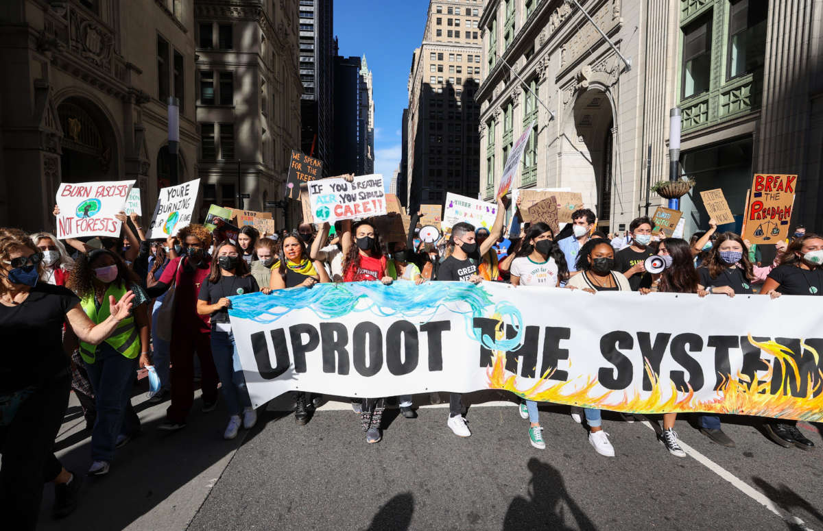 Climate change protesters march in New York City with banner reading Uproot the System