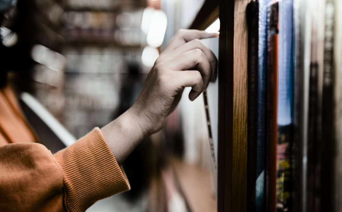 A hand pulls a book out from a library shelf