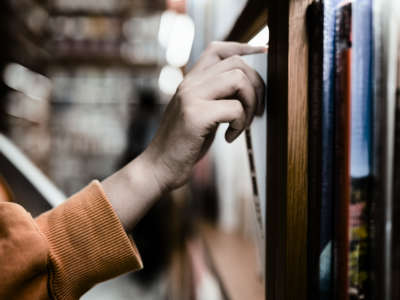 A hand pulls a book out from a library shelf