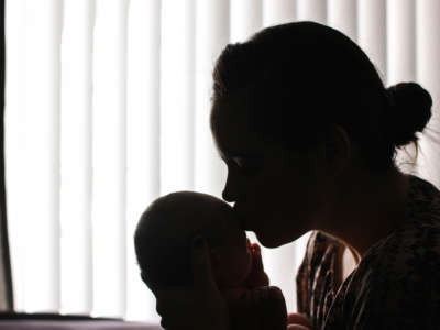 Mother kissing newborn baby's head in silhouette