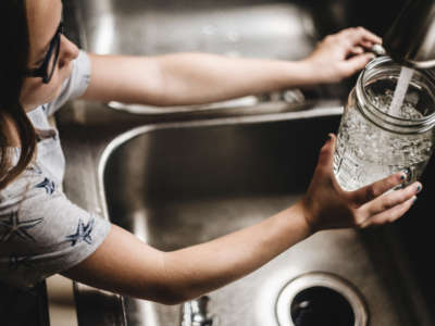 Child pours water from faucet into glass jar for drinking