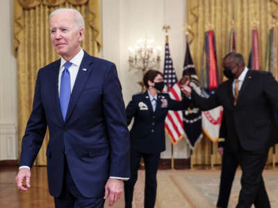 President Joe Biden walks out of the podium after speaking during International Women's Day in the East Room of the White House in Washington, D.C., on March 8, 2021. Behind Biden, Defense Secretary Lloyd Austin and Air Force General Jacqueline Van Ovost greet each other with an elbow-bump.