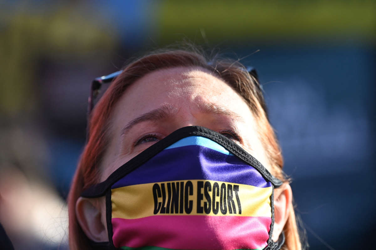 A protester wears a mask over their mouth and nose that reads "CLINIC ESCORT"