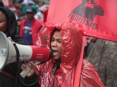 A protester in a red poncho speaks into a megaphone at an outdoor protest in the snow