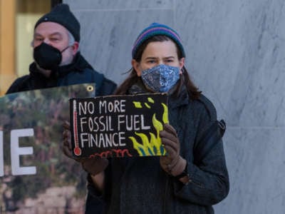 A protester holds a sign reading "NO MORE FOSSILE FUEL FINANCE" during a protest