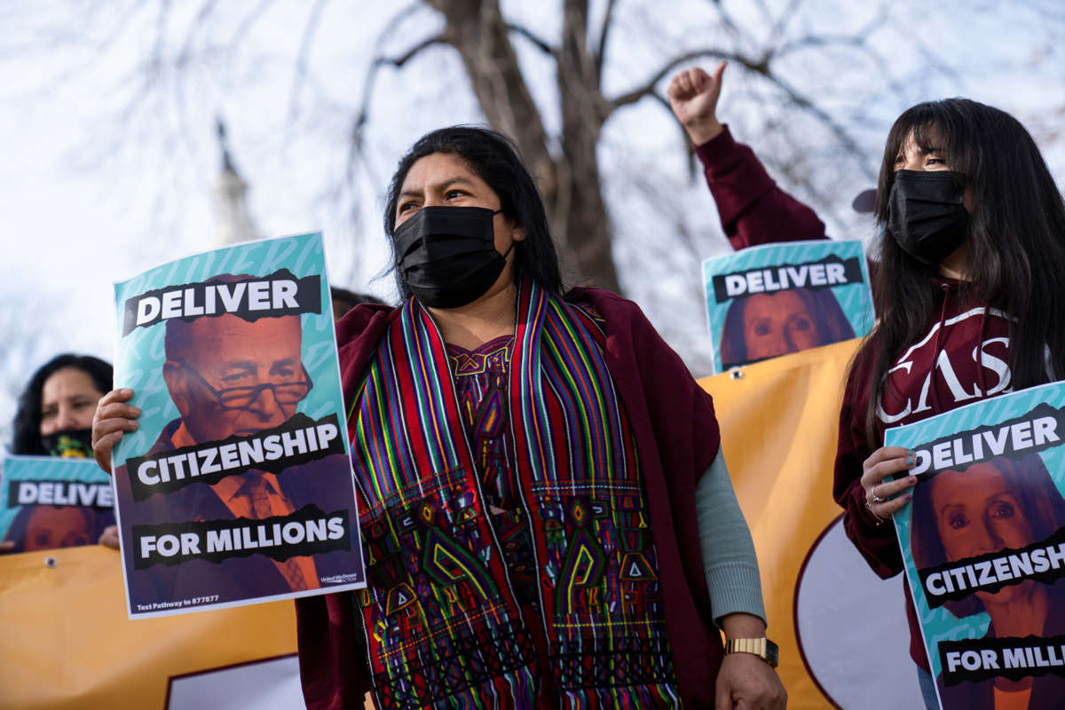 People in masks display signs bearing Sen. Chuck Schumer's face and reading "DELIVER CITIZENSHIP FOR MILLIONS"
