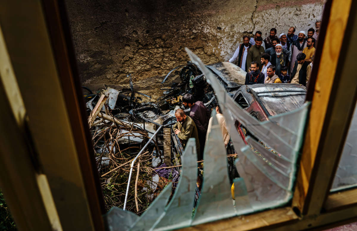 Relatives and neighbors of the Ahmadi family gather around the incinerated husk of a vehicle targeted and hit by an American drone strike that killed 10 civilians including 7 children, in Kabul, Afghanistan, on August 30, 2021.