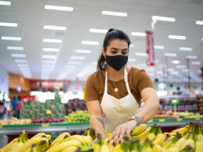 Grocery store worker wearing mask arranges bananas