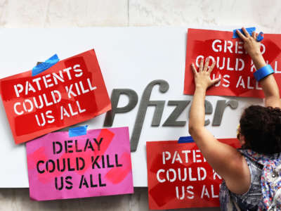 A woman tapes protest signs to the Pfizer sign during a protest at the Pfizer Pharmaceuticals Headquarters on July 14, 2021, in Manhattan in New York City.