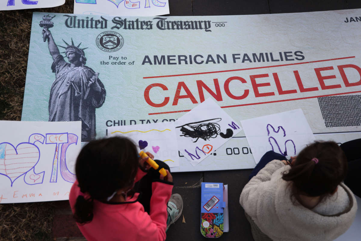 Children draw on top of a cancelled check prop during a rally in front of the U.S. Capitol on December 13, 2021, in Washington, D.C.