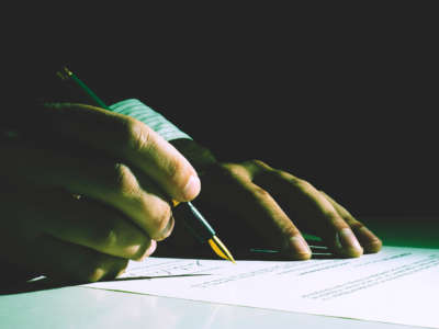 Hands of person in business suit sign paperwork in shadowy light