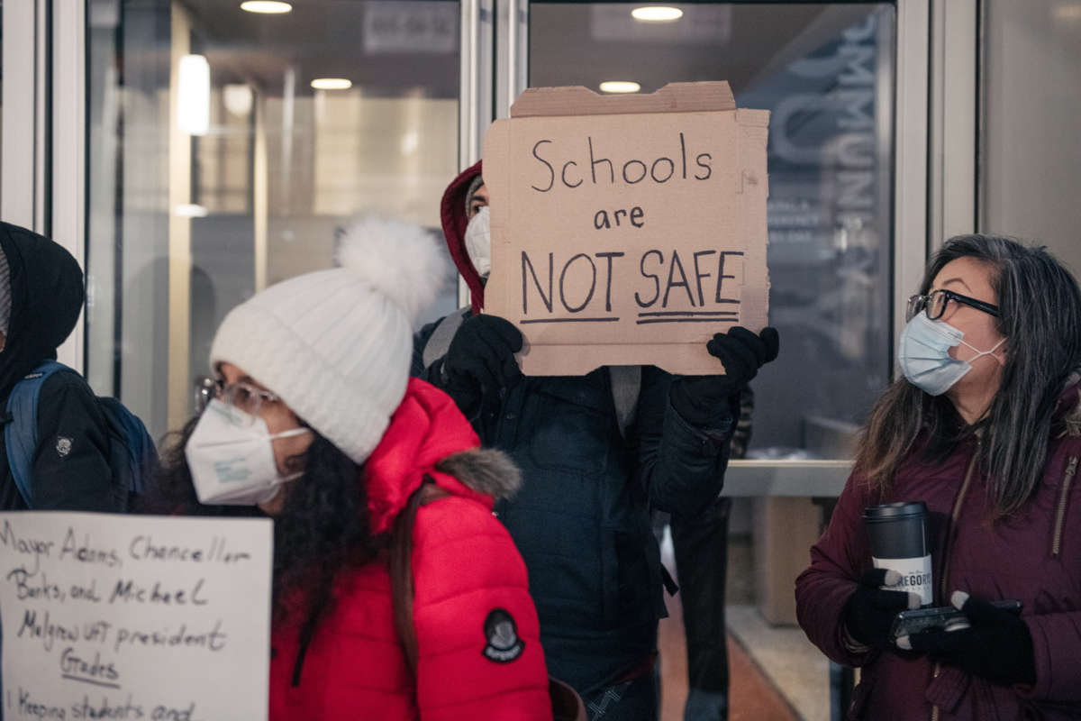 A masked protester holds up a sign reading "SCHOOLS ARE NOT SAFE" during an outdoor protest