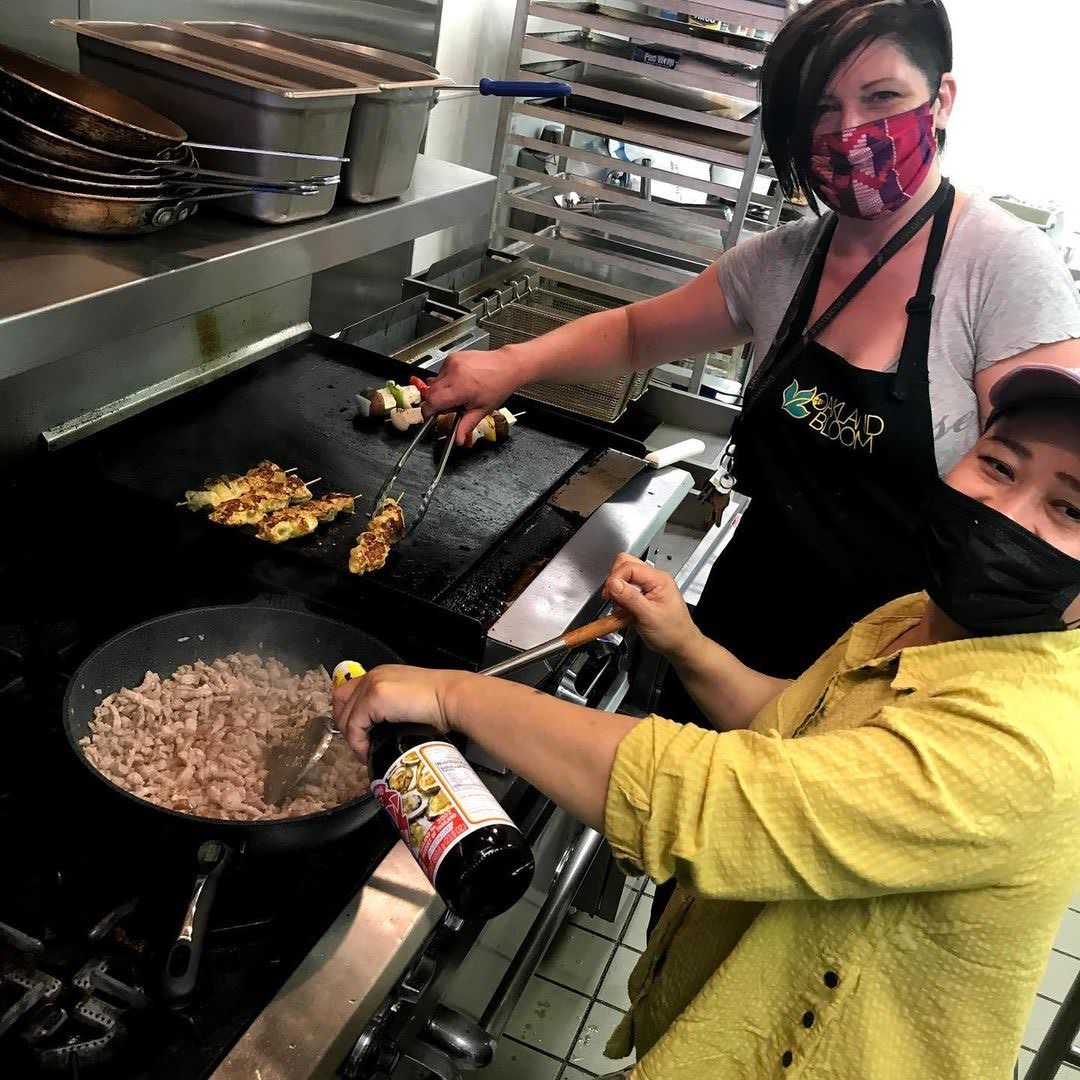 Oakland Bloom chefs Sanela and Pa Wah at the grill during their collaboration pop-up. Sanela grills turmeric chicken skewer and Pa Wah sautés Burmese-style Pad Kra Pao (a spicy pork and basil stir-fry).