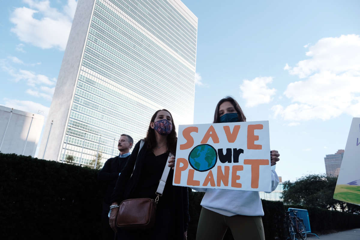 A masked protester holds a sign reading "SAVE OUR PLANET" during a protest outside the United Nations building