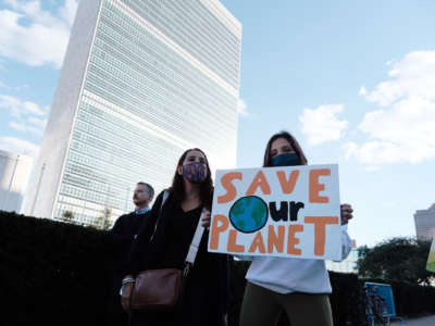 A masked protester holds a sign reading "SAVE OUR PLANET" during a protest outside the United Nations building