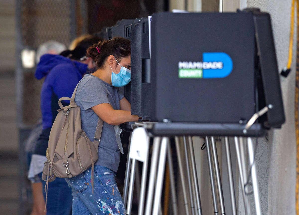 A woman in a medical mask votes at a booth
