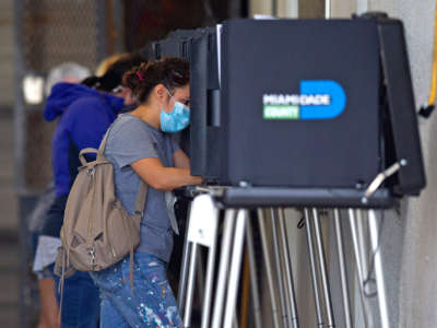 A woman in a medical mask votes at a booth