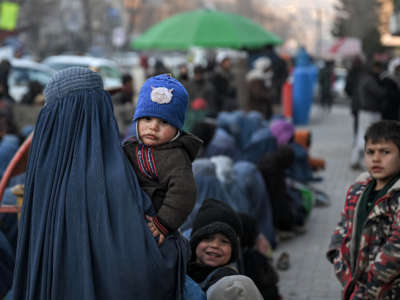 A woman wearing a burqa carries an infant as she waits with others for free bread in front of a bakery in Kabul, Afghanistan, on January 24, 2022.