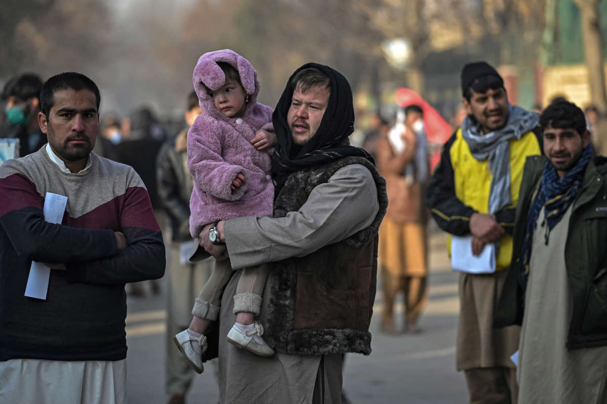 A man carries his daughter as people queue to enter the passport office at a checkpoint in Kabul, Afghanistan, on December 19, 2021.