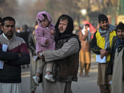 A man carries his daughter as people queue to enter the passport office at a checkpoint in Kabul, Afghanistan, on December 19, 2021.