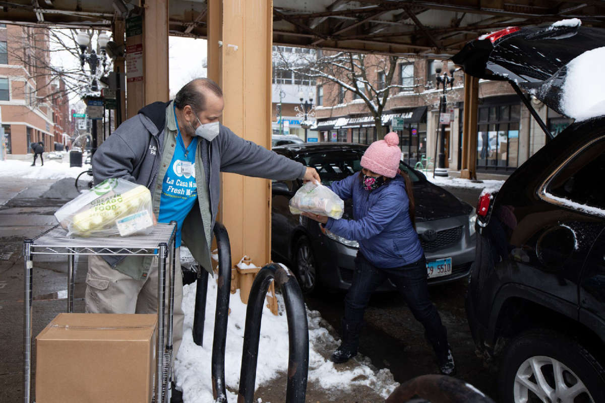 A volunteer with Lakeview Pantry helps a person load grocery items into a car outside the pantry on January 24, 2022, in Chicago's Lakeview neighborhood.