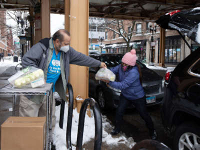 A volunteer with Lakeview Pantry helps a person load grocery items into a car outside the pantry on January 24, 2022, in Chicago's Lakeview neighborhood.