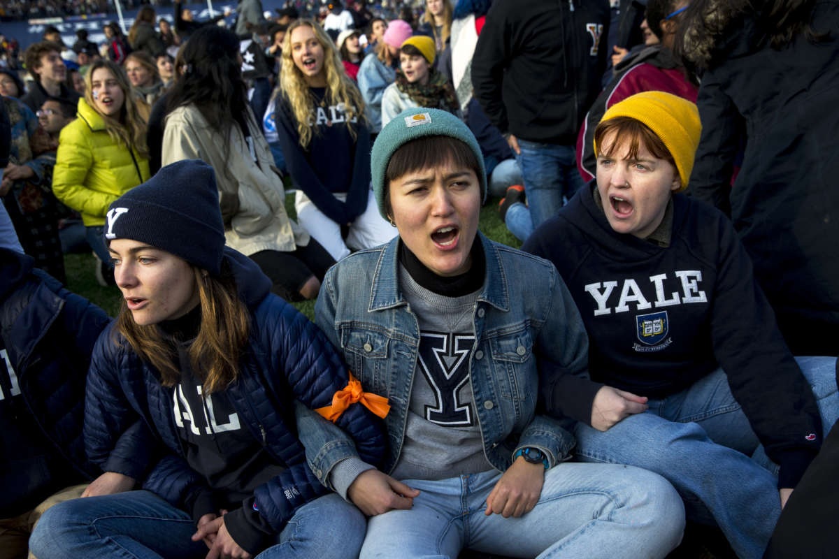 From left, Yale senior Nadia Grisaru, senior Sarah Adams and sophomore Lillian Burton protest during the halftime of the college football game between Harvard and Yale in New Haven, Connecticut, on November 23, 2019. Demonstrators stormed the field during halftime to demand both universities divest from fossil fuels.