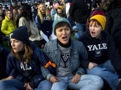 From left, Yale senior Nadia Grisaru, senior Sarah Adams and sophomore Lillian Burton protest during the halftime of the college football game between Harvard and Yale in New Haven, Connecticut, on November 23, 2019. Demonstrators stormed the field during halftime to demand both universities divest from fossil fuels.