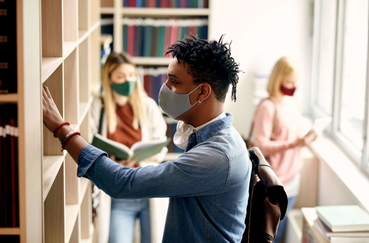 Teenage students looking at library books and wearing face masks