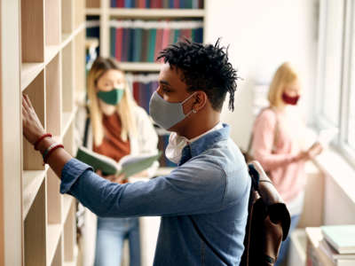 Teenage students looking at library books and wearing face masks