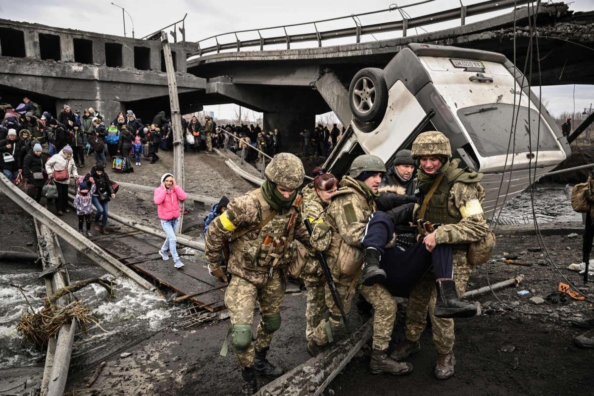 Ukrainian servicemen assist a person while people cross a destroyed bridge as they evacuate the city of Irpin, northwest of Kyiv, during heavy shelling and bombing on March 5, 2022, 10 days after Russia launched a military invasion on Ukraine.