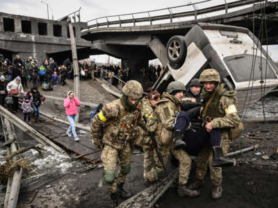 Ukrainian servicemen assist a person while people cross a destroyed bridge as they evacuate the city of Irpin, northwest of Kyiv, during heavy shelling and bombing on March 5, 2022, 10 days after Russia launched a military invasion on Ukraine.