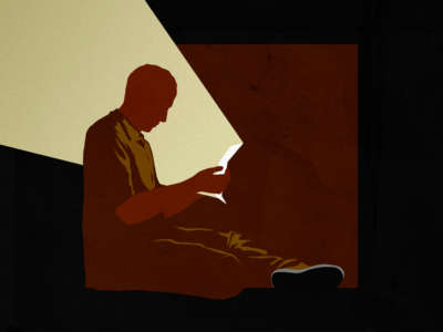 Prisoner reading letter, shining a light up at him and through the darkness around cell