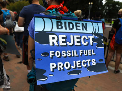 Climate protestor in Washington D.C. with a sign that says "Biden, reject fossil fuel projects"