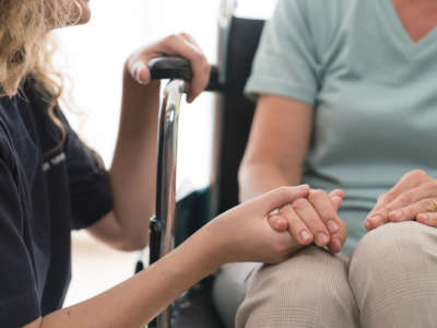 Young home nurse holding hands of senior woman in wheelchair.