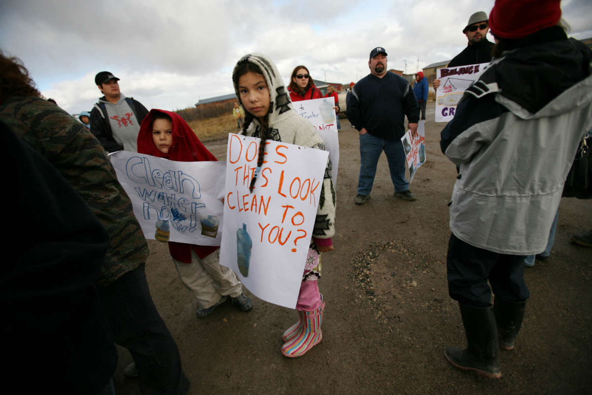 Young First Nations girl holding a sign with a bottle of dirty water on it that says "Does this look clean to you?"