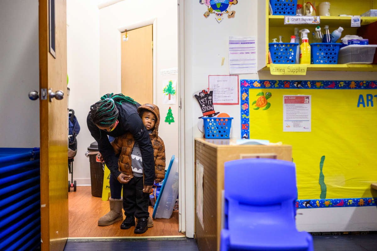 A teacher helps zip up a little boy's coat