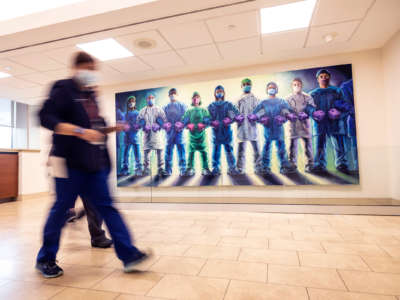 People hurriedly walk past a mural depicting health care workers linking arms